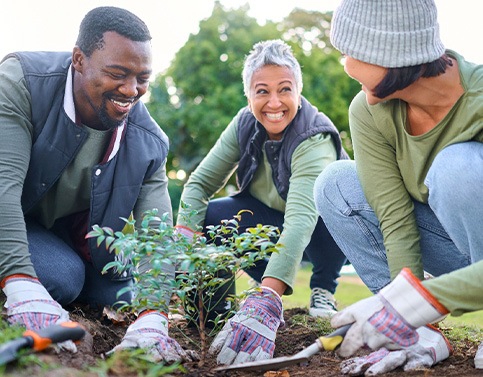 Group of volunteers smiling while planting a tree