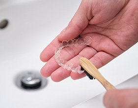 Patient using toothbrush to clean aligners in sink