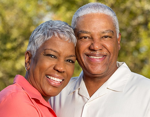 Smiling man and woman after all on 4 tooth replacement