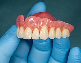 A closeup of an upper denture held by a gloved hand