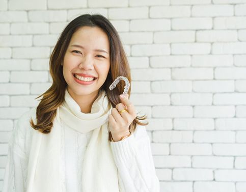 woman in white sweater holding aligner for Invisalign in Edison 