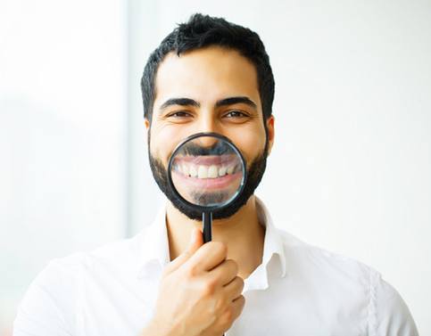 man holding magnifying glass to his straight white teeth 