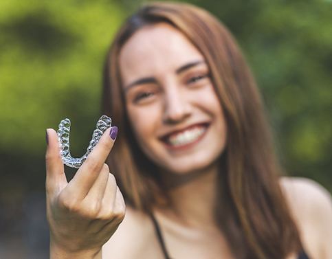 Woman smiling while holding Invisalign aligner