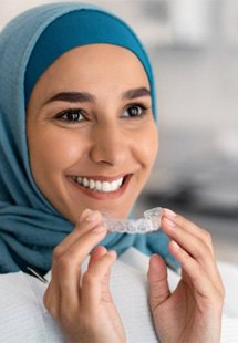 : a woman smiling while holding Invisalign aligners