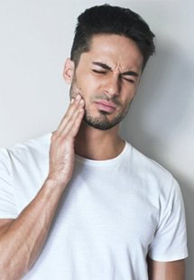 : a man touching his jaw due to tooth pain