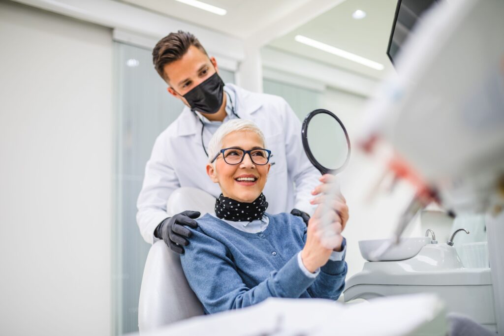 Woman in dental chair smiling at reflection with dentist touching her shoulders