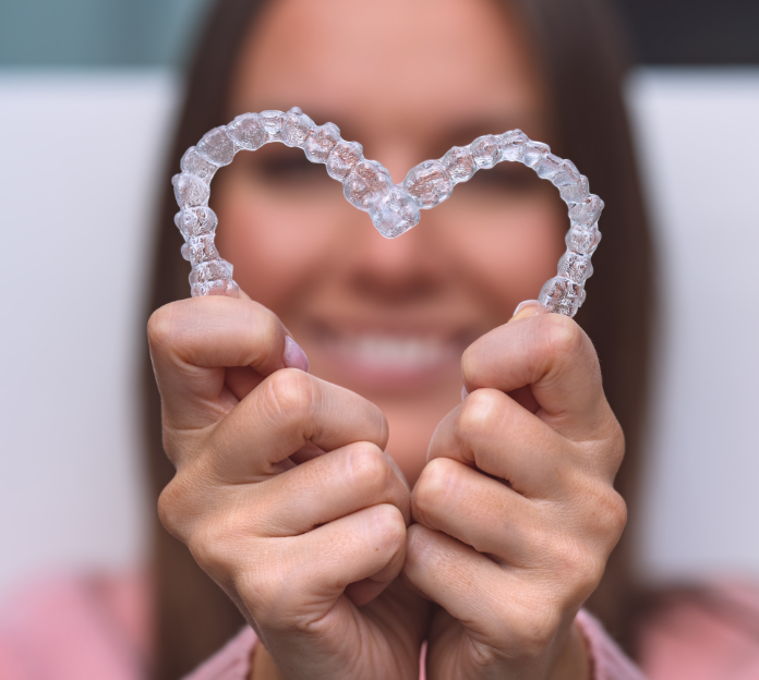 Woman holding clear aligners in heart shape.