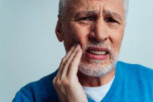 Senior man with dentures holding face in pain.